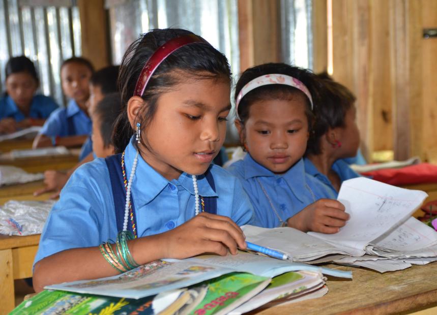 Two young girls reading something in a school in Asia supported by our mission.